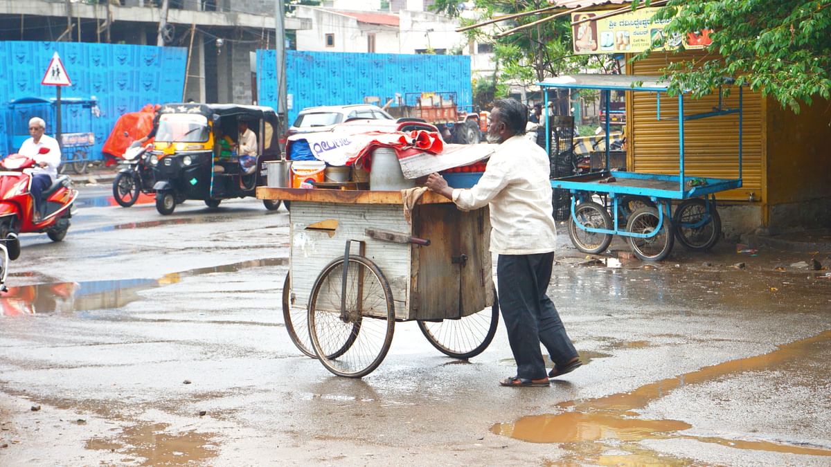 ಸಣ್ಣಗೆ ಸುರಿಯುತ್ತಿದ್ದ ಮಳೆಯ ನಡುವೆಯೂ ವ್ಯಾಪಾರದ ಬಂಡಿ ತಳ್ಳುತ್ತಿದ್ದ ವ್ಯಕ್ತಿ 
ಚಿತ್ರ: ಮುರುಳಿಕಾಂತರಾವ್‌ 