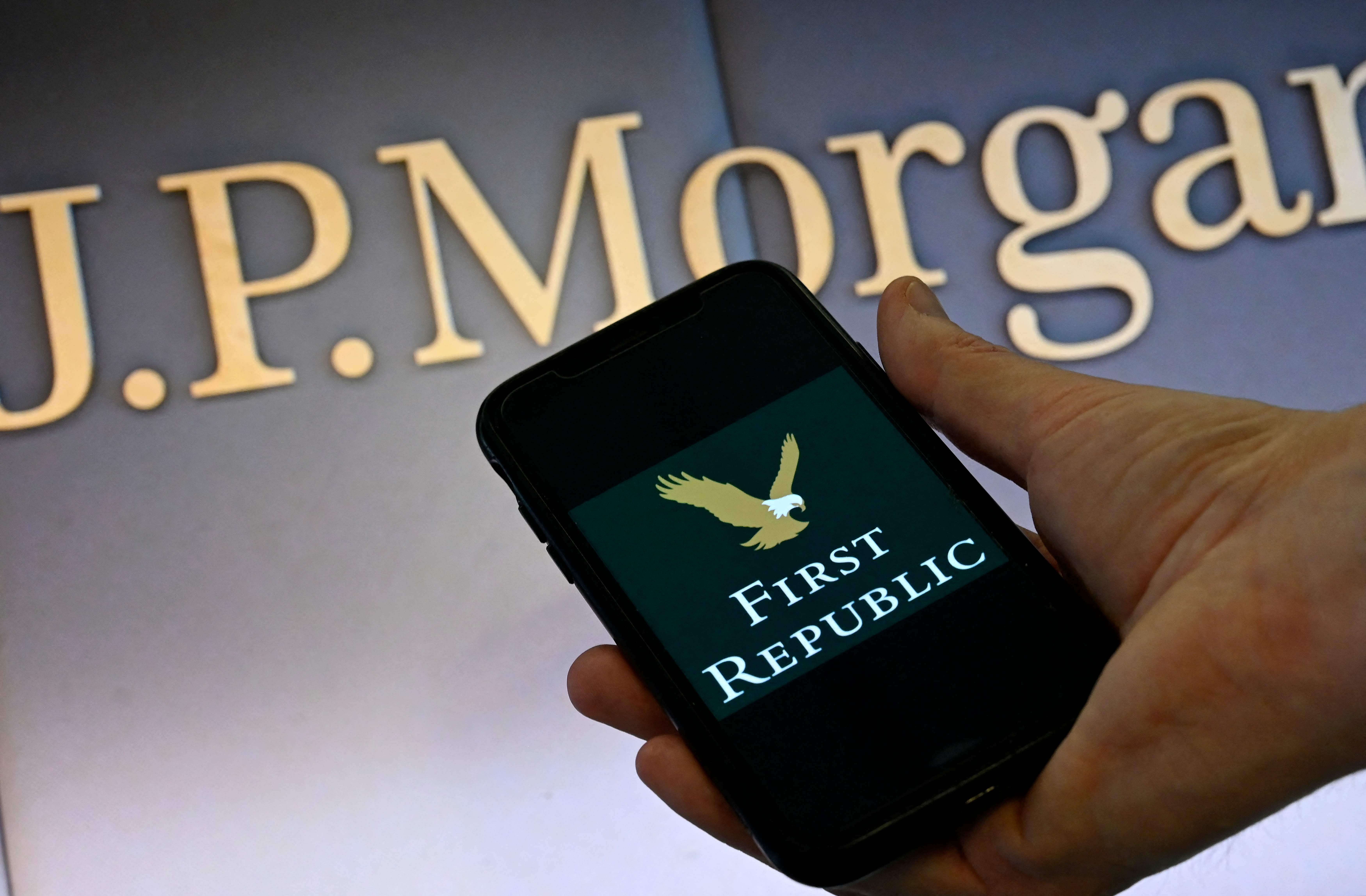 This illustration photo shows a smart phone screen displaying the logo of First Republic Bank, with a screen showing the logo of JP Morgan Chase in the background in Washington, DC on May 01, 2023. - US financial authorities seized California's troubled First Republic Bank on Monday and sold it to JPMorgan Chase, hoping to bring to a close a two-month banking crisis that has spooked the financial system. (Photo by OLIVIER DOULIERY / AFP)