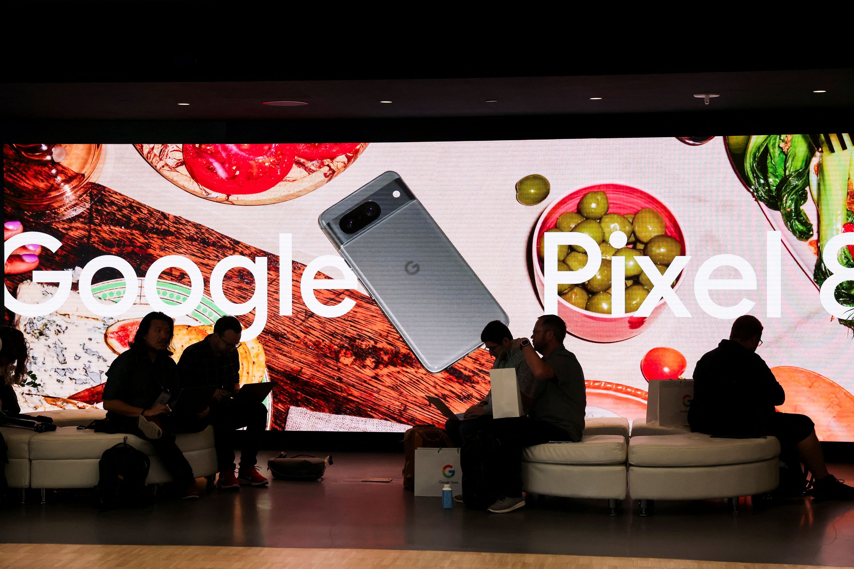 People sit in front of an ad for a new Google Pixel 8 Phone in New York City, U.S., October 4, 2023. REUTERS/Caitlin Ochs