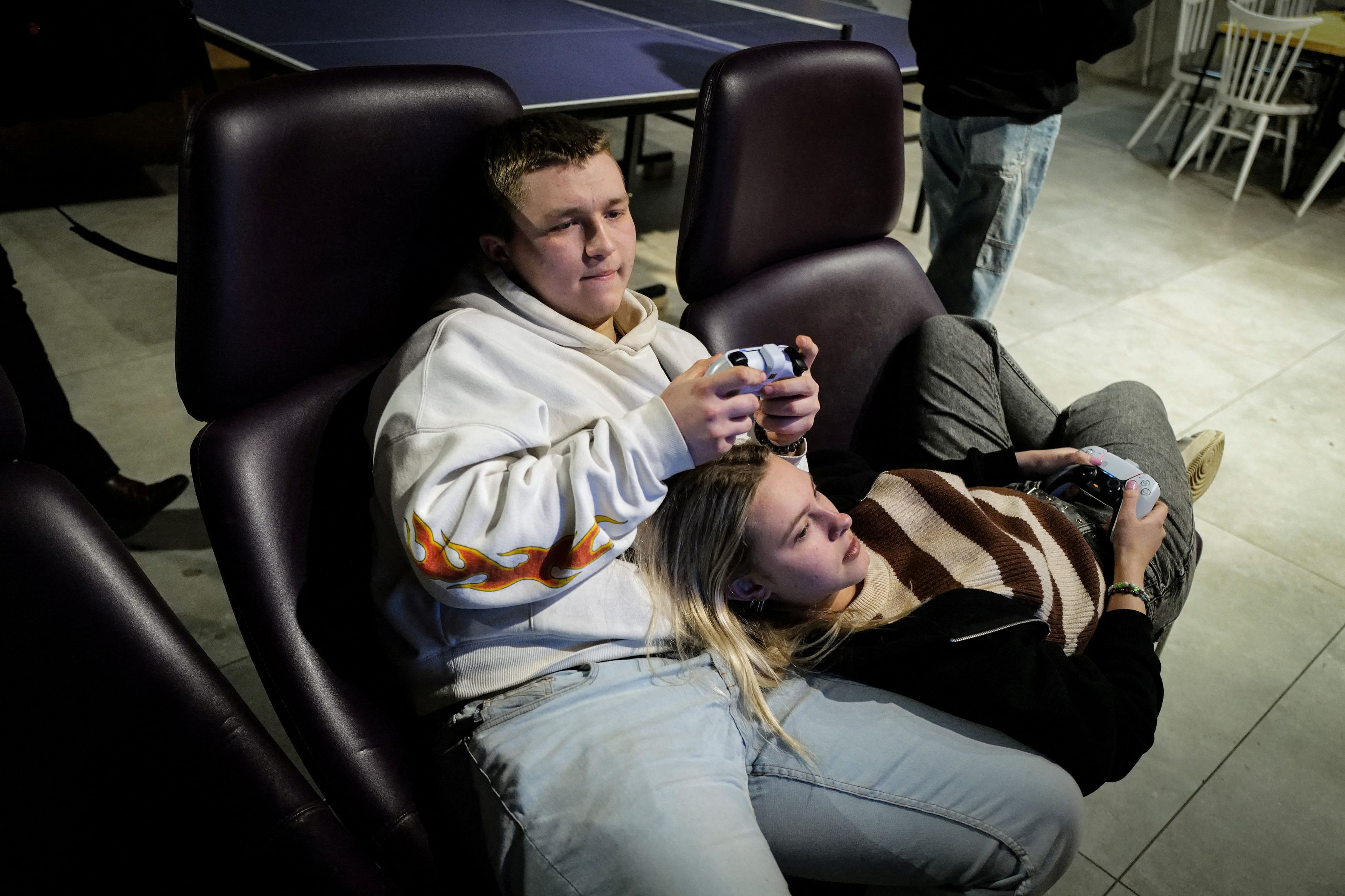 Dariia Vynohradova, 17, from Kharkiv and her boyfriend Dmytro Demchevskyi, 18, from Yuzhnoukrainsk, play a video game at Blue Trainers.