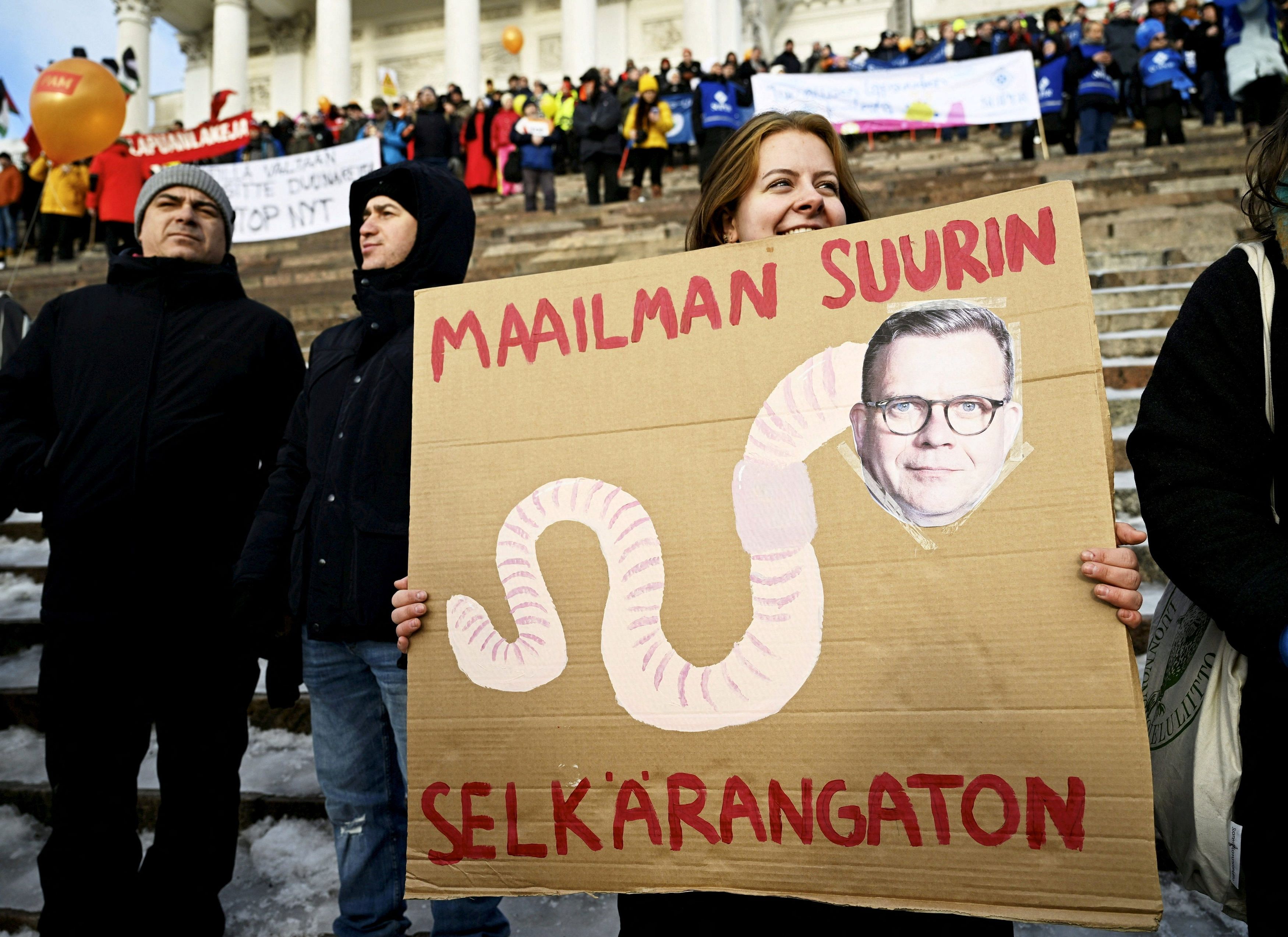 <div class="paragraphs"><p>Liisa Huhtala holds a banner with Finland's PM Petteri Orpo's face attached to a body of a worm at the Stop Now! demonstration against Finland's government.</p></div>