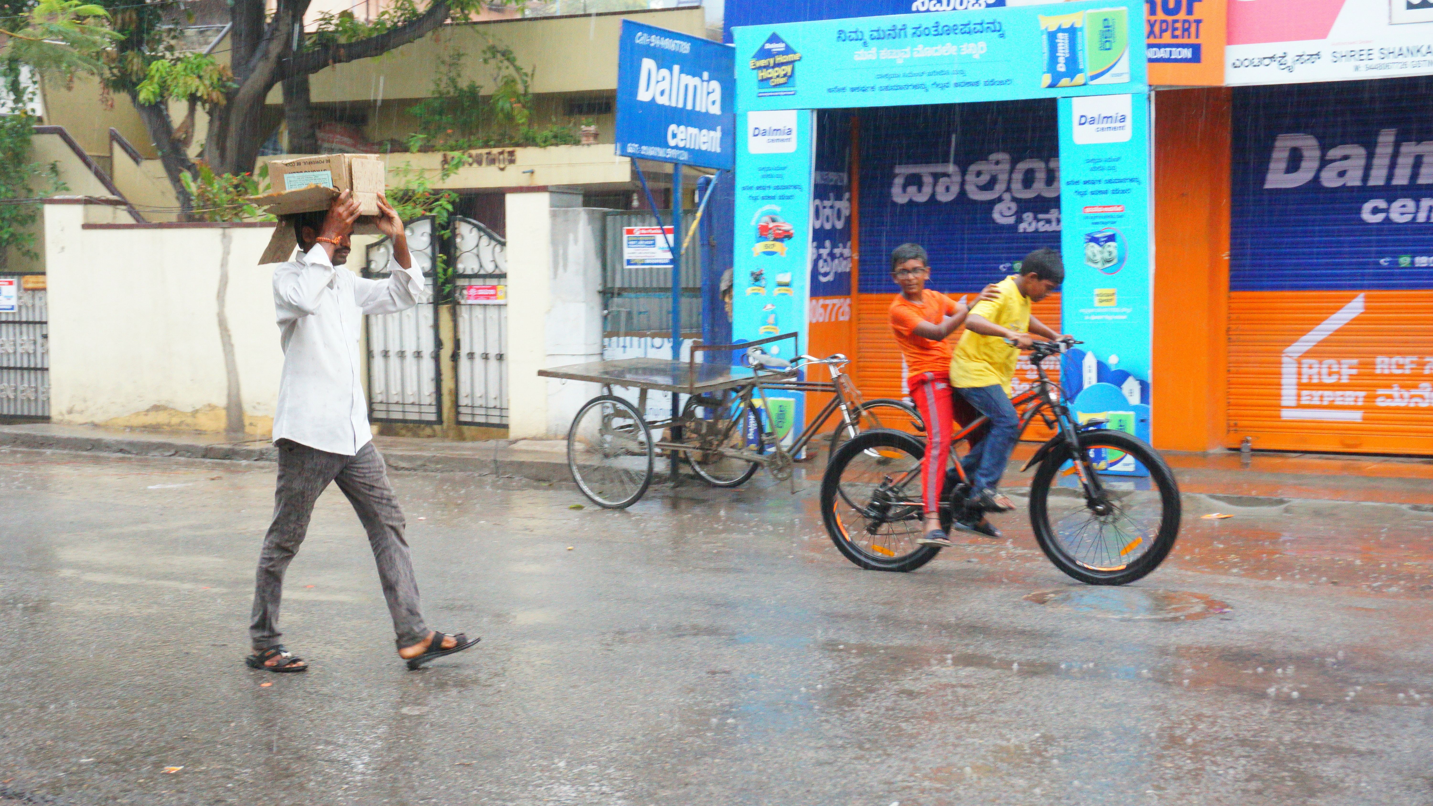 ಬಳ್ಳಾರಿ ನಗರದಲ್ಲಿ ಭಾನುವಾರ ಸುರಿದ ಮಳೆಯಲ್ಲಿ ವ್ಯಕ್ತಿಯೊಬ್ಬರು ಡಬ್ಬದ ರಕ್ಷಣೆ ಪಡೆದು ಸಾಗುತ್ತಿರುವುದು. ಮತ್ತೊಂದೆಡೆ ಮಕ್ಕಳು ಮಳೆಯಲ್ಲಿ ಸೈಕಲ್ ಓಡಿಸಿ ಸಂಭ್ರಮಿಸಿದರು