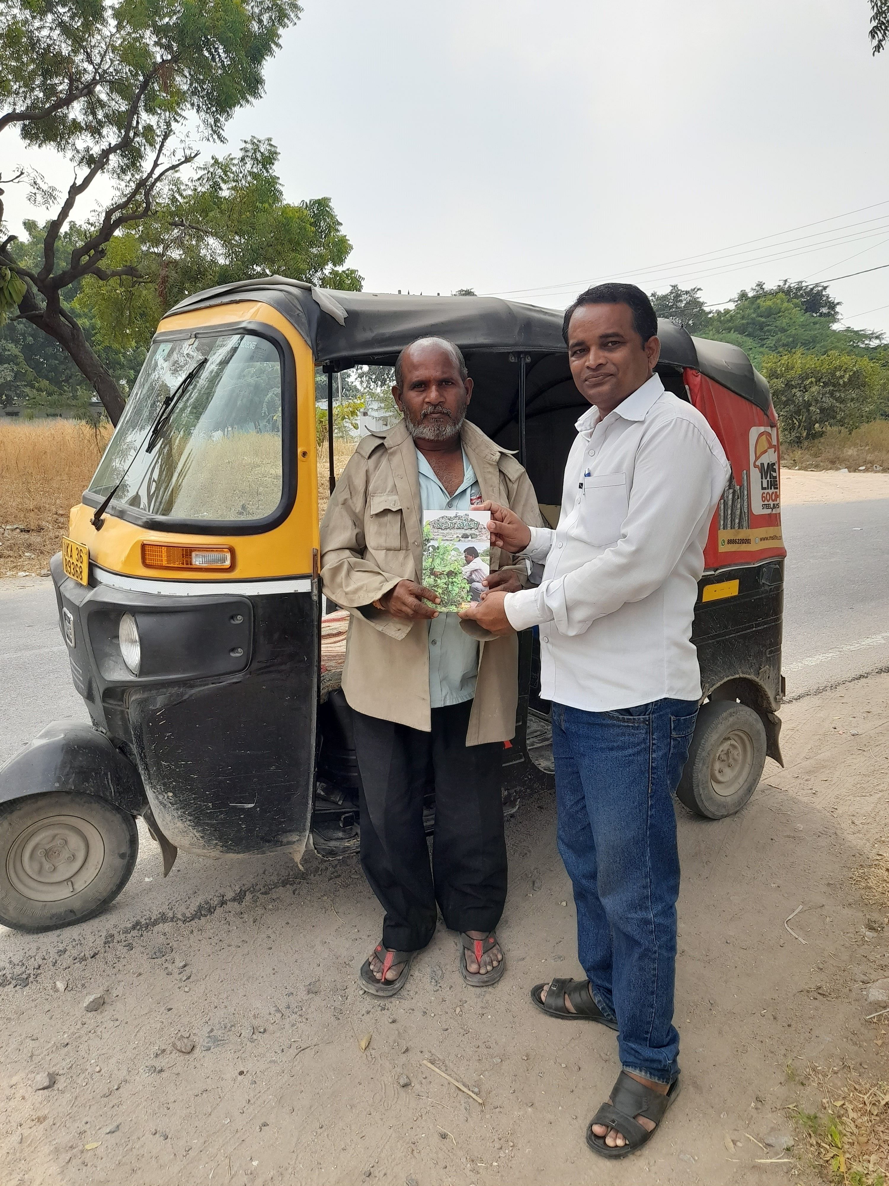 ರಾಯಚೂರಿನ ಆಟೊ ಚಾಲಕರೊಬ್ಬರಿಗೆ ಈರಣ್ಣ ಬೆಂಗಾಲಿ ಕನ್ನಡ ಪುಸ್ತಕ ನೀಡುತ್ತಿರುವುದು