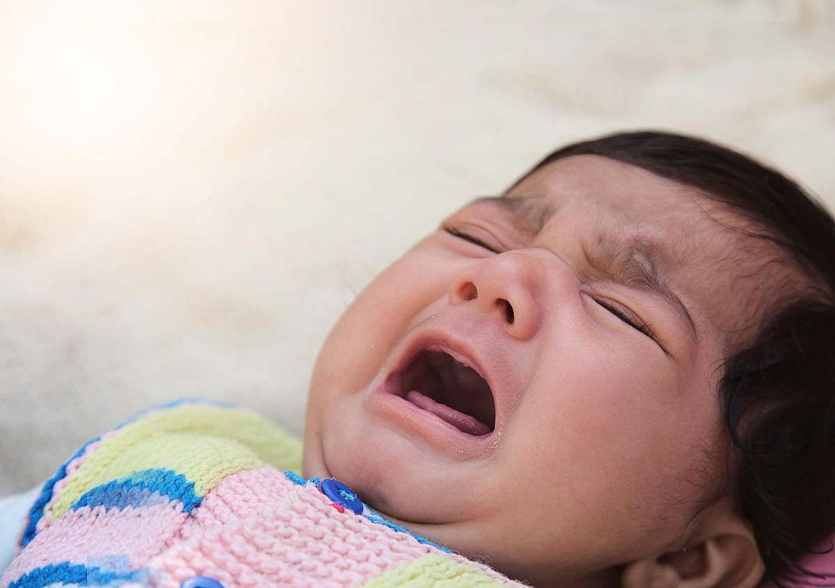 Crying infant in white blanketಅಳುವ ಮಗು