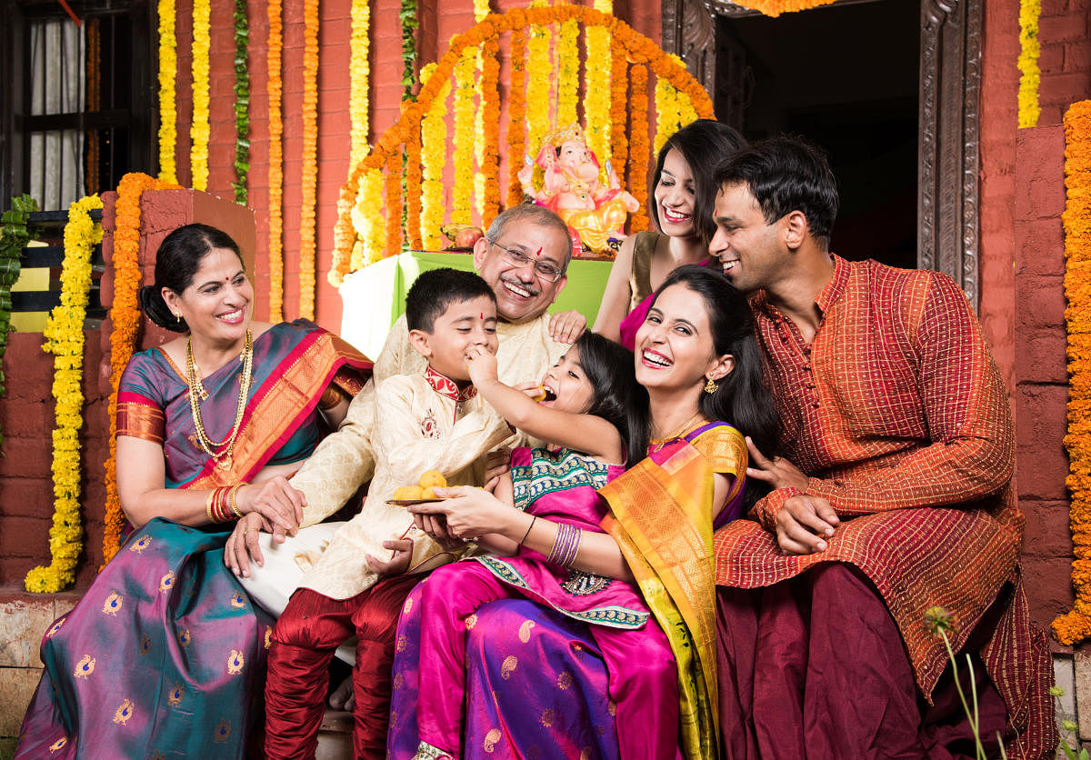 group photo of cheerful indian family eating sweet meets or laddu on ganesh festival, happy indian family and ganpati festival celebration