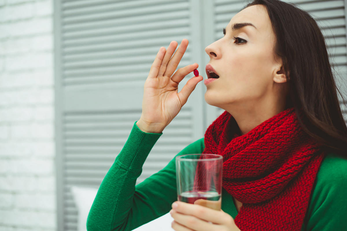 Reception of medicines. Photo of a young woman in a red scarf on the bed at home that keeps the tablet in his hand and glass of water. The concept of health and disease.