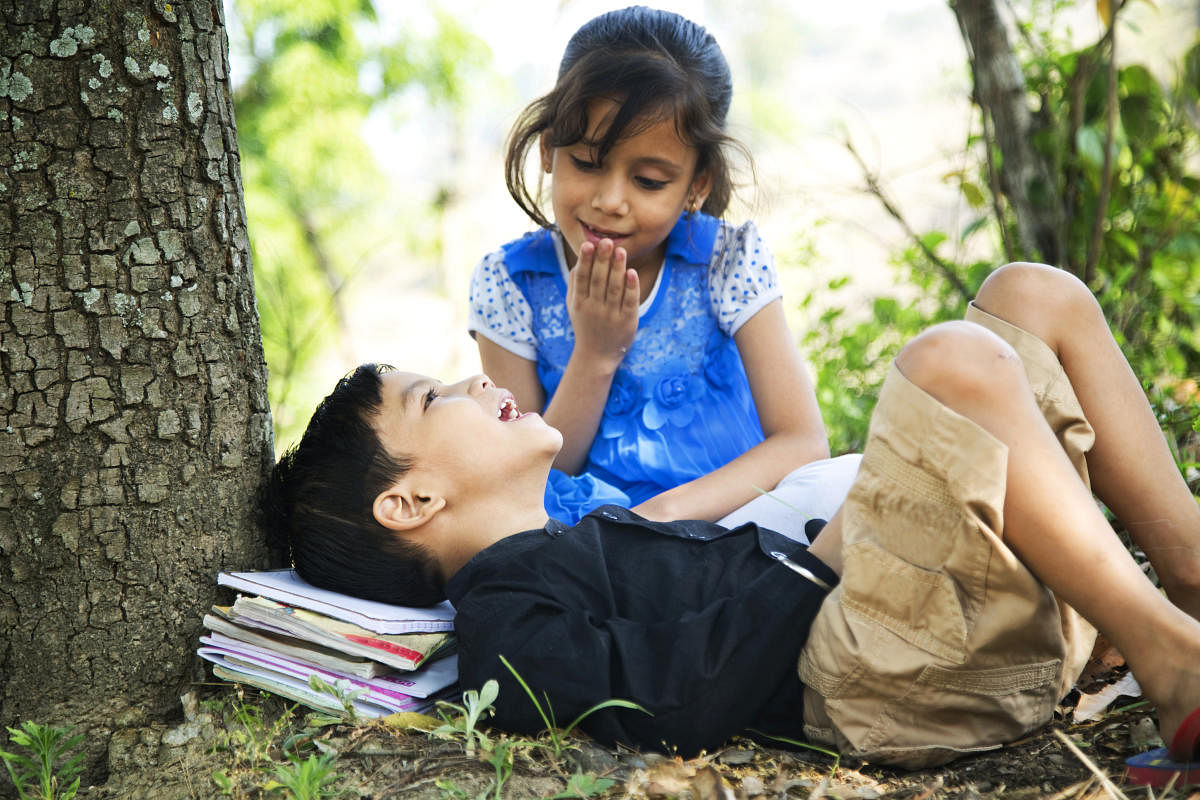 Boy lying under tree with his sister and smiling