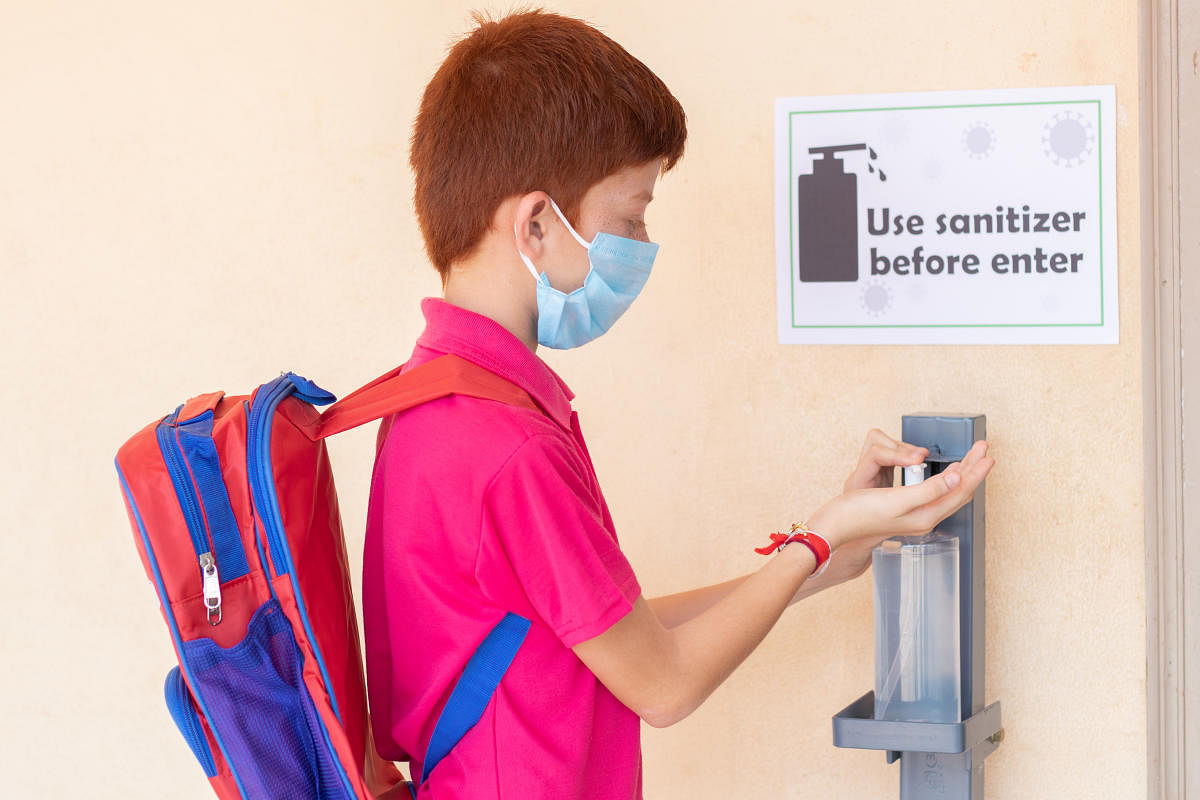 Kid with medical mask using hand sanitizer before entering classroom - concept of back to school or school reopen and coronavirus or covid-19 safety measures.Kid with medical mask using hand sanitizer before entering classroom - concept of back to school or school reopen and coronavirus or covid-19 safety measures.