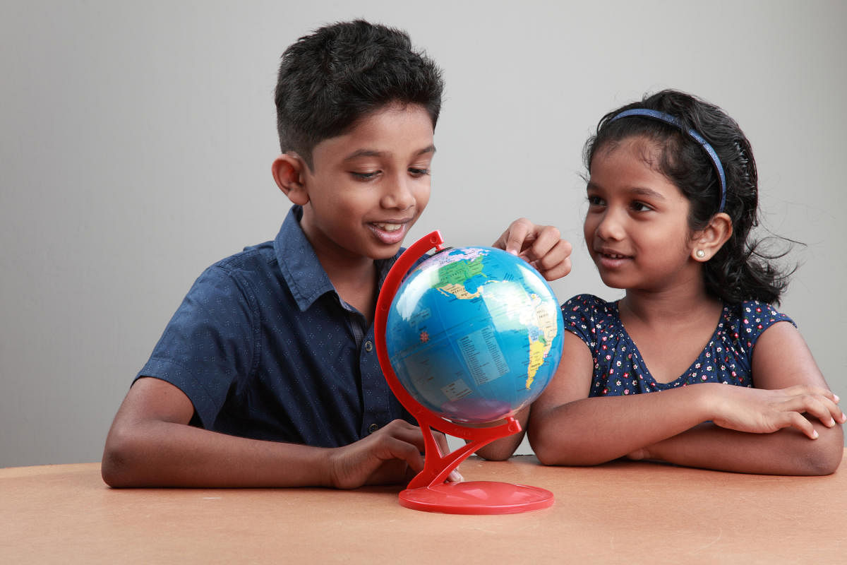 Little boy and girl look at the globe on a study tableBoy and girl with a globe