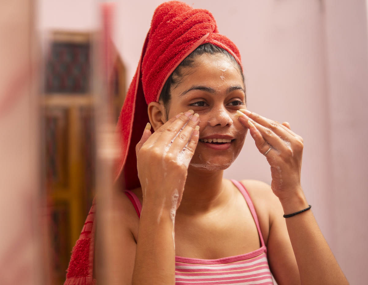 beautiful girl wearing a towel on head front of mirror and washing her face with organic face wash.Girl wearing towel on head and washing face.