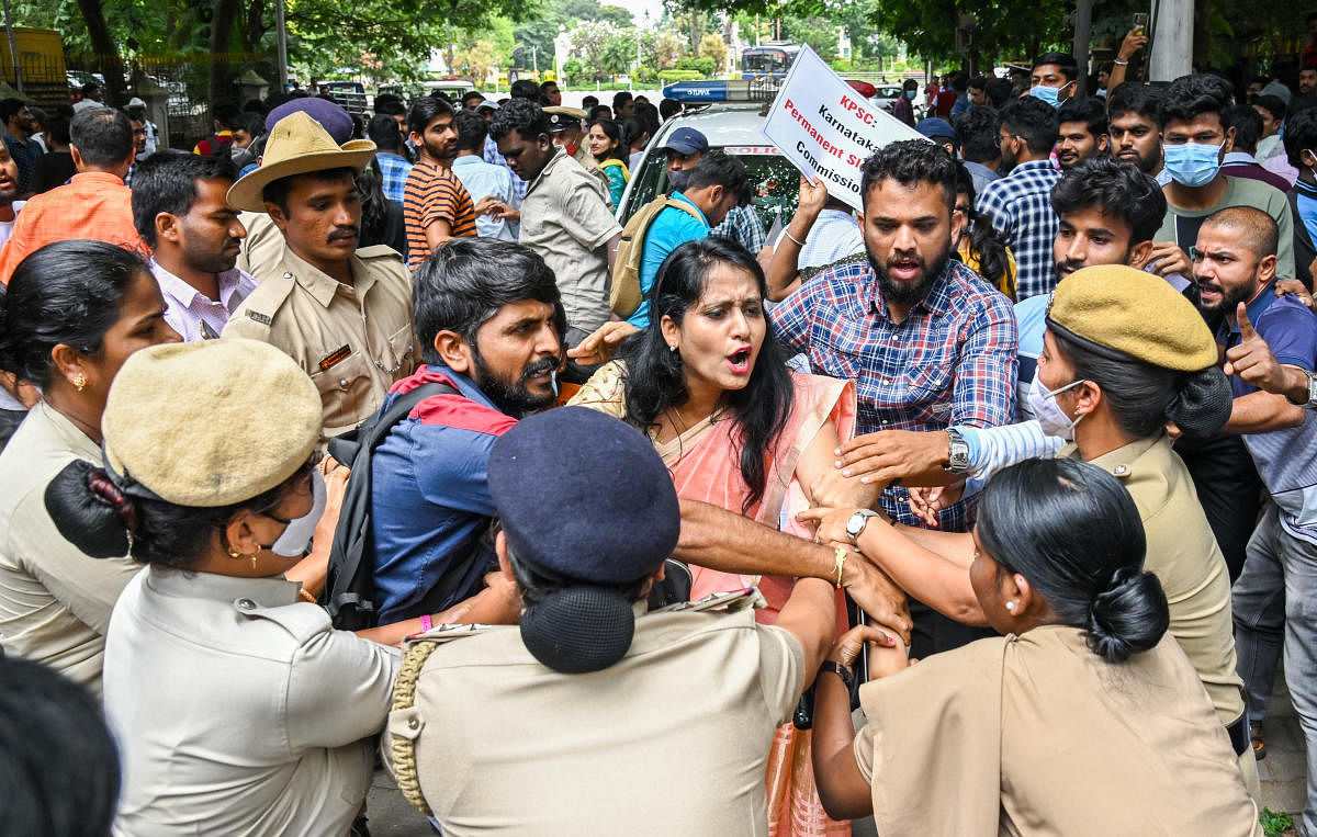 ಕೆಪಿಎಸ್‌ಸಿ ಪ್ರವೇಶದ್ವಾರದ ಬಳಿ ಪ್ರತಿಭಟನೆ ನಡೆಸಿದ ಭವ್ಯಾ ನರಸಿಂಹಮೂರ್ತಿ ಮತ್ತು ಉದ್ಯೋಗಾಕಾಂಕ್ಷಿಗಳನ್ನು ಪೊಲೀಸರು ವಶಕ್ಕೆ ಪಡೆದರು –ಪ್ರಜಾವಾಣಿ ಚಿತ್ರ